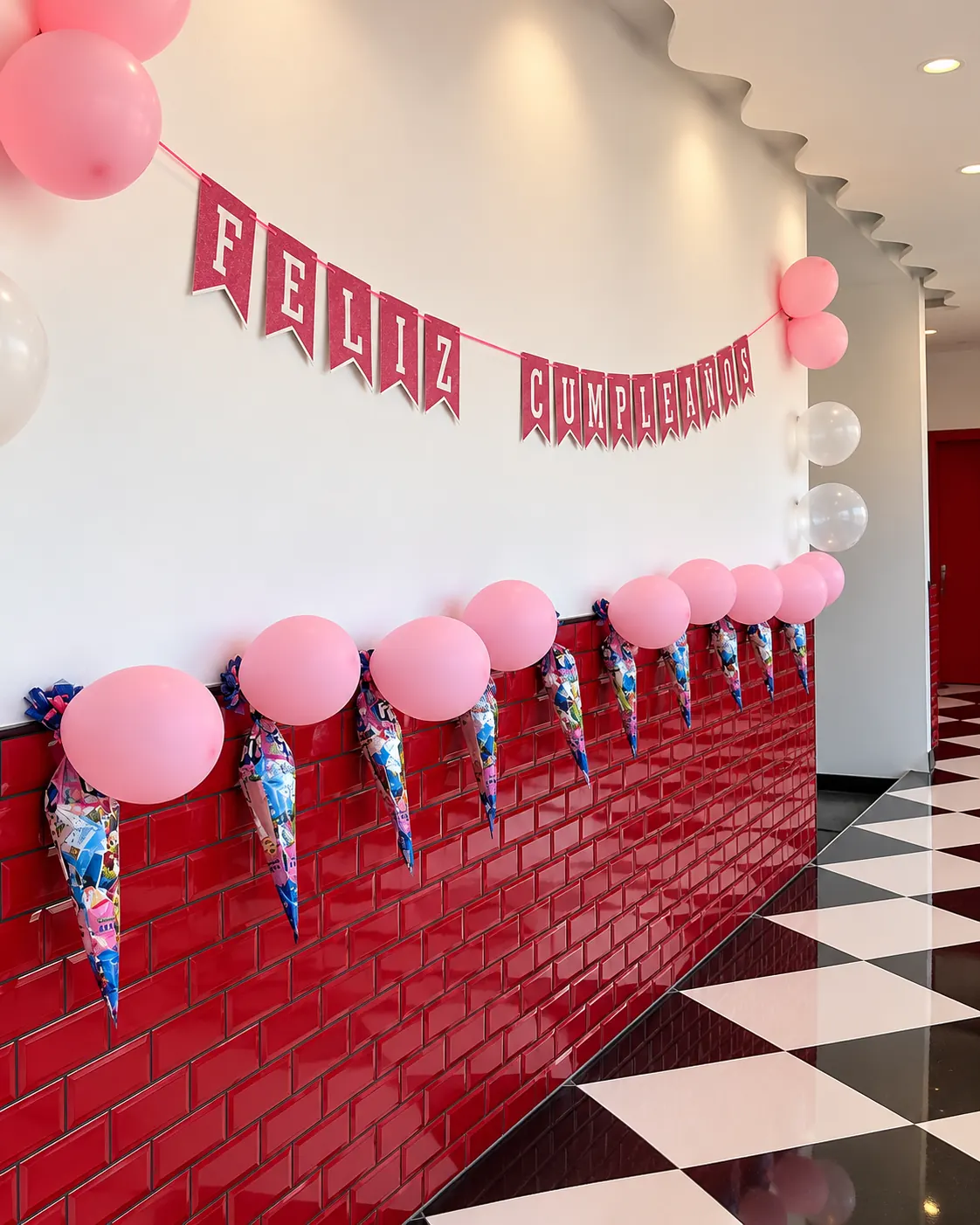 Salón de Ruta 67 decorado para un cumpleaños: guirnalda de Feliz cumpleaños, globos rosas y conos de chuches